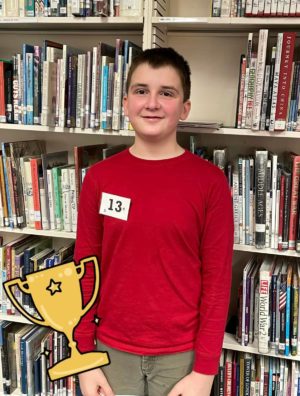 Timothy Clince, Champion of the 2022 Helena Middle School Spelling Bee, stands in front of shelves of books in the school library
