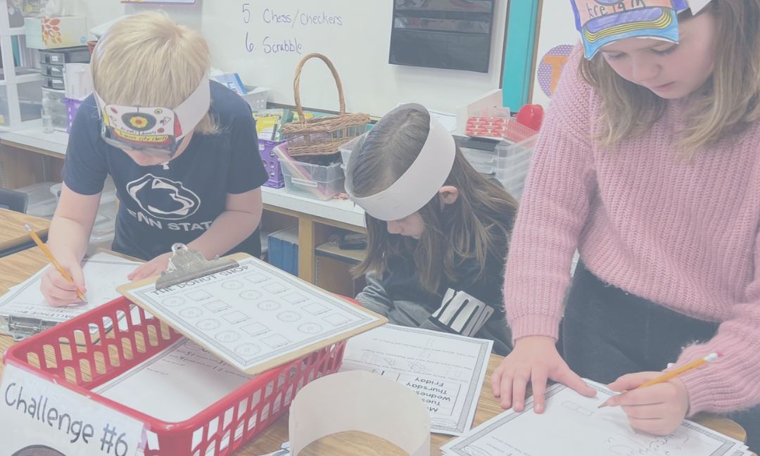 Elementary students bent over a table working on a lesson with clipboards.