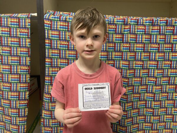 An elementary-aged boy holds his "Nugget of Kindness" Certificate